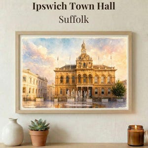 May include: A framed watercolor print of Ipswich Town Hall in Suffolk. The artwork depicts a grand, ornate building with a clock tower, fountains, and surrounding buildings. The sky is a blend of blue, pink, and yellow hues. The text "Ipswich Town Hall Suffolk" is at the top.