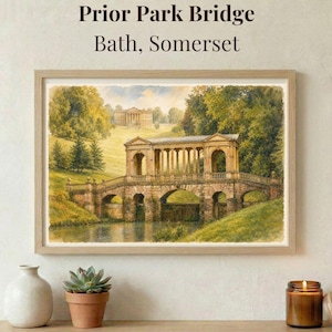 May include: A framed watercolor print of Prior Park Bridge in Bath, Somerset. The artwork depicts a stone bridge with arches and columns, set in a lush green landscape with a building in the background. The print is in a light wooden frame.