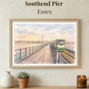 Może przedstawiać: Oprawiony wydruk akwareli Southend Pier w Essex, z zielonym pociągiem na molo. Dzieło sztuki w jasnej drewnianej ramie przedstawia molo rozciągające się w wodzie pod kolorowym niebem z napisem "Southend Pier Essex".