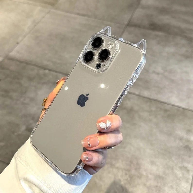 May include: Clear phone case with cat ear design. The case is transparent, allowing the phone's color to show through. The case has a sleek, modern design with a playful touch, featuring small cat ears at the top.