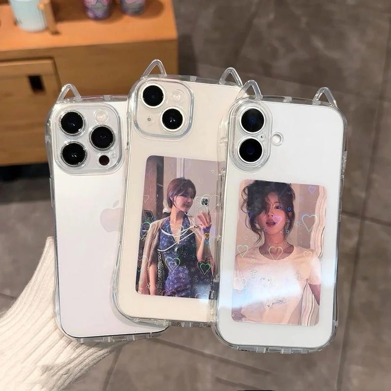 May include: Three clear phone cases with cat ear accents. Two cases feature photos of a person, and one is plain. The cases are designed to fit a smartphone and have a clear, protective design.