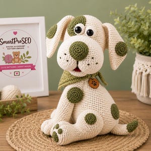 Peut inclure: Un chien en crochet de couleur crème avec des taches vert olive foncé sur les oreilles, le corps et les pattes. Le chien a de grands yeux noirs en plastique, un nez rond olive et porte un bandana vert olive assorti avec une breloque patte.