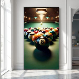 May include: A framed print of a pool table with a full rack of billiard balls. The black 8-ball is in the foreground. The balls are arranged in a triangle on a green felt surface. Overhead lights illuminate the scene.