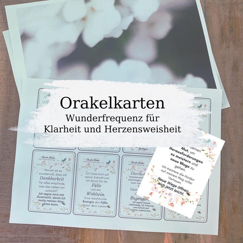 May include: A set of oracle cards with the text "Orakelkarten Wunderfrequenz f&uuml;r Klarheit und Herzensweisheit". The cards have floral designs and inspirational quotes. The image has a soft, blurred background.