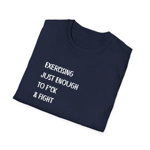 May include: Navy blue t-shirt with white text that reads: EXERCISING JUST ENOUGH TO F*CK & FIGHT. The shirt is folded and displayed on a white background. The t-shirt is a crew neck style.