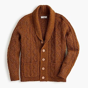 Op de afbeelding: Een bruin kabelgebreid vest met een sjaalkraag en houten knopen. De trui heeft twee voorzakken en een textuurpatroon. Het label is zichtbaar aan de binnenkant van de kraag.