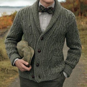 May include: A green cable-knit cardigan with dark brown buttons and a shawl collar. The cardigan is worn over a collared shirt and a plaid bow tie. A tweed cap is held in the hand.
