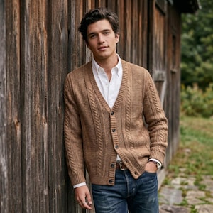 May include: A tan cable-knit cardigan with a V-neckline and dark buttons, worn over a crisp white button-down shirt paired with dark blue denim jeans. The knit sweater features vertical cable patterns along the front and long sleeves.