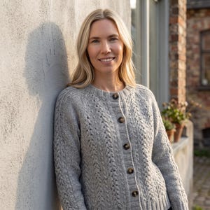 Può includere: Un cardigan in maglia grigio chiaro con motivo a trecce verticali, scollo rotondo e cinque bottoni marrone scuro sul davanti. Il capo presenta maniche lunghe con polsini e orlo a coste, realizzato in filato testurizzato.