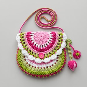 Puede incluir: Un bolso bandolera redondo de ganchillo con una paleta de colores vibrantes en hilo rosa, verde lima y blanco. El bolso tiene un borde festoneado blanco, un cierre central de botón rosa, una correa larga y dos colgantes decorativos.