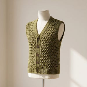 May include: An olive green sleeveless vest featuring a V-neckline and a front button closure with five dark brown buttons. The garment is crafted with a textured, open-knit crochet pattern and includes a ribbed border along the neckline and hem.