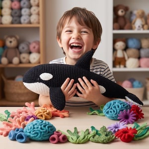May include: A black and white crocheted orca plush toy held by a person, surrounded by a collection of colorful crocheted sea life elements including coral, sea anemones, and seaweed in shades of blue, green, pink, red, and orange.