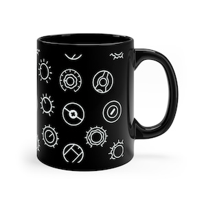May include: Black ceramic mug with a repeating pattern of white geometric shapes. The shapes include circles, sunbursts, and other abstract designs. The mug has a curved handle and a glossy finish.