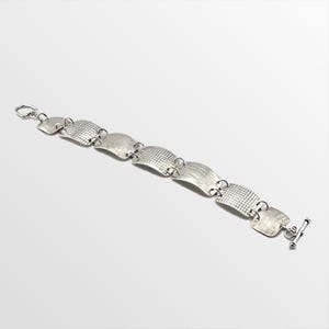 May include: A silver bracelet with a series of connected, textured rectangular links. The links alternate between a crosshatch and a linear pattern. The bracelet has a toggle clasp and a small loop closure.