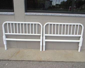 May include: Two white, vintage-style bed headboards. Each headboard features a spindle design with turned posts and a horizontal rail. The headboards are painted white and are displayed against a neutral-colored wall.