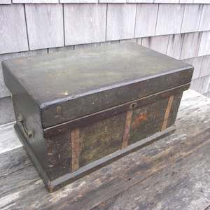 May include: A vintage wooden box with a dark green paint finish and metal accents. The box has a hinged lid and a metal handle on the side.
