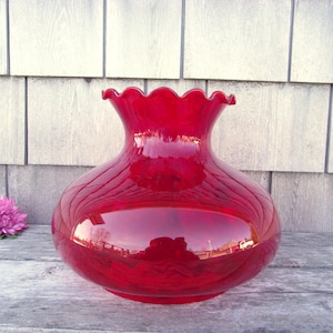 May include: A deep red glass lampshade with a scalloped rim. The shade is round and has a slight bulbous shape.