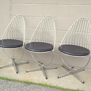 May include: Three chrome and black swivel chairs with a unique, curved, wire frame design. The chairs have black vinyl seats and a star-shaped base.