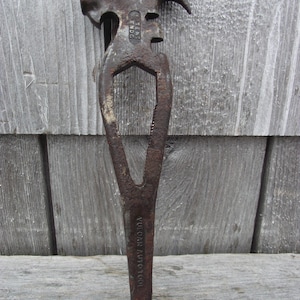 May include: An antique, rusty metal tool with a hammer head, claw, and a long, pointed handle. The tool has the text "VULCAN AUTO TOOL" and "PATENT ENDOG" stamped on it. The tool is set against a weathered wooden background.