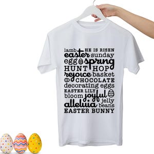 May include: White t-shirt with the words "lamb, easter, egg, spring, hunt, rejoice, chocolate, decorating eggs, Easter Lily, bloom, joyful, alleluia, jelly beans, Easter Bunny" printed in black. The shirt is hanging on a white hanger. Colorful Easter eggs are at the bottom.
