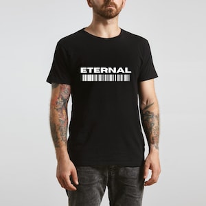 Puede incluir: Camiseta negra con la palabra "ETERNAL" en blanco, sobre una serie de líneas verticales blancas. La camiseta es de cuello redondo. La persona lleva vaqueros grises.