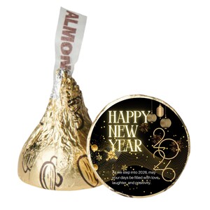 May include: A gold foil-wrapped Hershey's Kiss candy with an almond label, next to a black and gold Happy New Year 2026 sticker. The sticker includes the text "As we step into 2026, may your days be filled with love, laughter, and positivity."