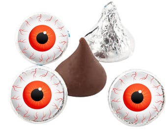 Puede incluir: Arreglo de dulces con temática de Halloween. La imagen muestra tres caramelos con un diseño de ojo, con iris rojo, pupila negra y venas rojas. También hay un beso de chocolate. El fondo es blanco.