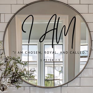 Puede incluir: Un espejo redondo con marco negro. Las palabras "I AM" están escritas en cursiva sobre el espejo. Debajo, el texto dice "I AM CHOSEN, ROYAL, AND CALLED." 1 PEDRO 2:9. El espejo refleja una ventana.