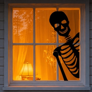 May include: A black skeleton silhouette decal applied to the glass of a window pane. The skeleton is positioned on the right side, showing the skull, rib cage, and one arm against the warm, orange-lit interior of a room with a lamp.