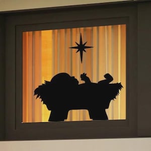May include: A black silhouette of the nativity scene, featuring the baby Jesus in a manger, with a star above. The background has vertical lines with a warm, golden glow, framed by a dark window.