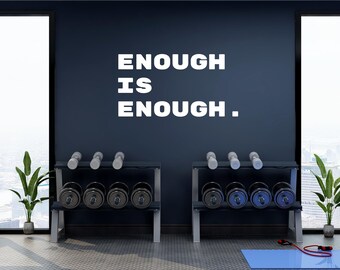May include: A gym interior with a dark blue wall featuring the white text "ENOUGH IS ENOUGH." Two dumbbell racks hold various weights. A blue exercise mat and a jump rope are on the floor. Potted plants flank the windows.