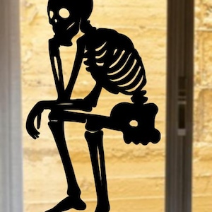 May include: A black silhouette of a skeleton in a seated position, with one hand supporting its head in a thoughtful pose. The skeleton is depicted with detailed rib cage and leg bones, perfect for Halloween decorations.