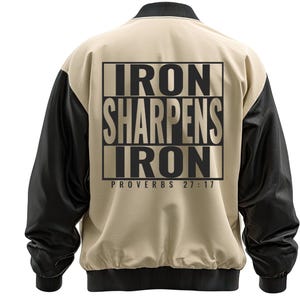 Könnte beinhalten: Beige und schwarze Collegejacke mit dem Text "IRON SHARPENS IRON PROVERBS 27:17" auf dem Rücken. Die Jacke hat schwarze Ärmel, einen schwarzen Kragen und Bündchen. Der Körper der Jacke ist beige.