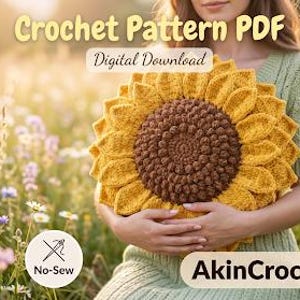 Op de afbeelding: Een gehaakt zonnebloemkussen met gele bloemblaadjes en een bruin centrum wordt vastgehouden voor een persoon in een veld met wilde bloemen. De tekst "Crochet Pattern PDF" en "Digital Download" zijn zichtbaar. De afbeelding bevat ook de tekst "No-Sew" en "AkinCrochetStore".