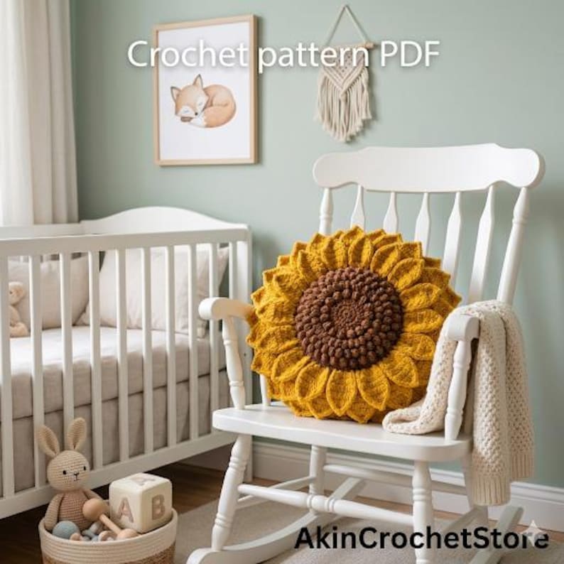 Op de afbeelding: Een gehaakt zonnebloemkussen in geel en bruin ligt op een witte schommelstoel. Een cr&egrave;mekleurige deken is over de arm van de stoel gedrapeerd. De tekst "Crochet pattern PDF" is zichtbaar in de afbeelding.