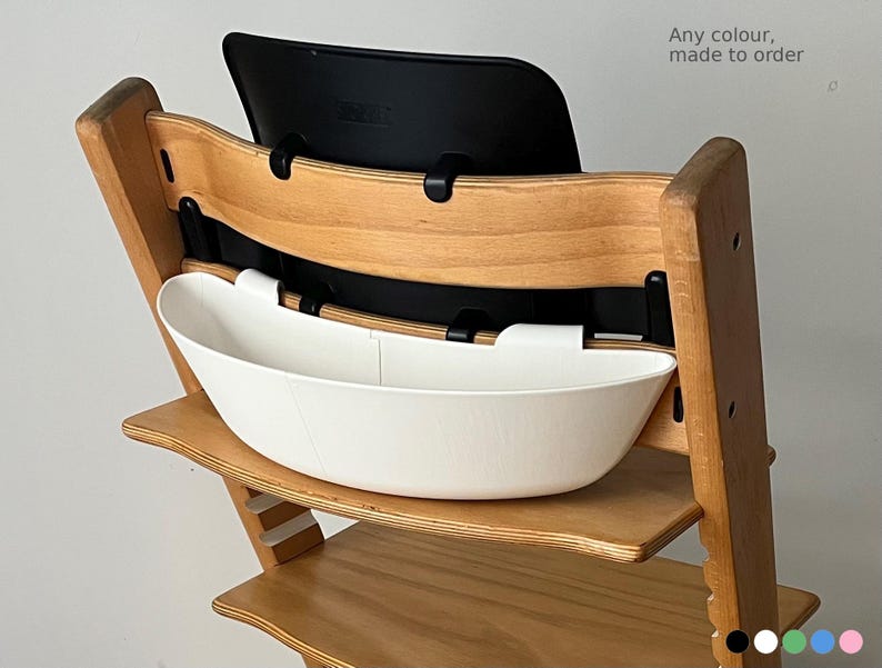 May include: Wooden high chair with a white plastic tray and black backrest. The text "Any colour, made to order" is visible. The chair is made of light-colored wood.