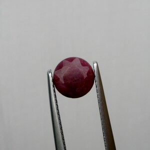 May include: A close-up of a red star-shaped gemstone held by tweezers.
