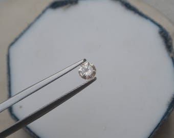 May include: A clear round diamond gemstone held by tweezers against a white background.