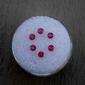 Pode incluir: Seis pedras preciosas redondas de cor vermelha são exibidas em uma superfície branca texturizada. As pedras preciosas estão dispostas em círculo.