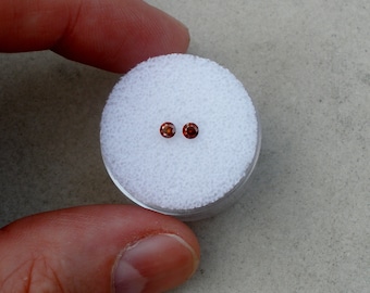 May include: Two small, round, orange gemstones in a white foam container.