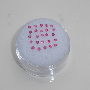 Puede incluir: Un recipiente de plástico transparente con un inserto de espuma blanca. El inserto tiene 25 pequeñas piedras preciosas rosadas dispuestas en una cuadrícula.