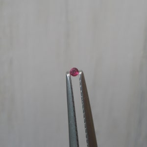 May include: A small, round, pink gemstone held in tweezers.