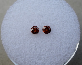 May include: Two round, dark red gemstones on a white background.