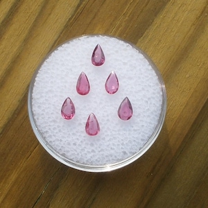 Può includere: Sei pietre preziose rosa a forma di goccia disposte su uno sfondo bianco.