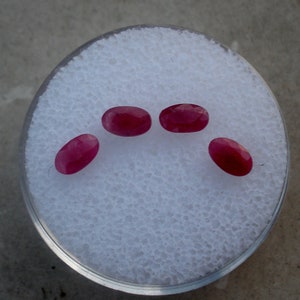May include: Four oval-shaped, deep red gemstones on a white background.