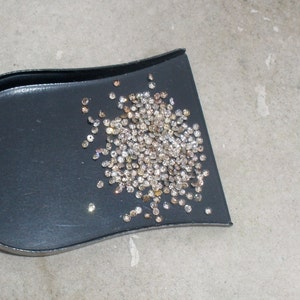 May include: A black scoop filled with a large quantity of small, clear, and brown diamonds.