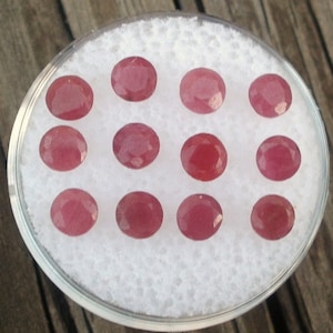 Puede incluir: Doce piedras preciosas ovaladas de color rosa dispuestas sobre un fondo blanco.