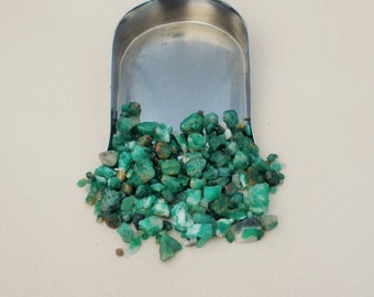May include: A silver scoop overflowing with small, green emerald gemstones. The gemstones are various shapes and sizes.