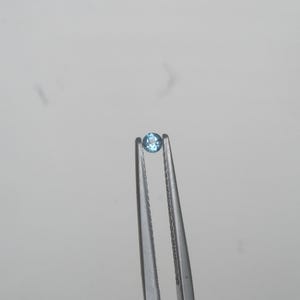 May include: A small, round, light blue gemstone held in tweezers.