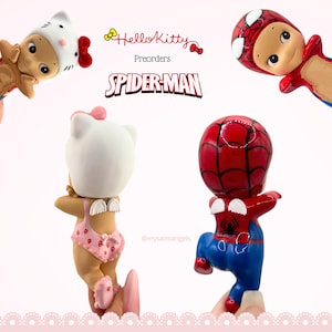 May include: Four small figurines featuring Hello Kitty and Spider-Man themes. The text reads Hello Kitty Preorders SPIDER-MAN and @mysaintangels. The figures include a Hello Kitty headpiece, a Spider-Man mask, and small white wings on their backs.